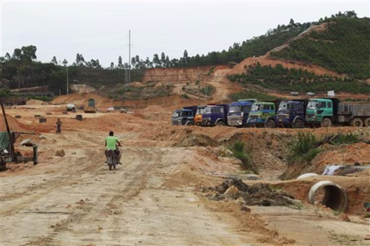 Workers ride their motorcycles by dump trucks at a construction site by Minmetals Land Ltd., the real estate development arm of China Minmetals Corp., China's largest metals trader, in Boluo county, suburb of Huizhou city, Guangdong province, China, Friday, June 17, 2011. After taking photos and collecting other data on Hallstatt, Austria, while mingling with the tourists, the Chinese firm has started to rebuild much of the village in faraway Guandong province, a project that residents of the Austrian village see with mixed emotions. (AP Photo/Kin Cheung)